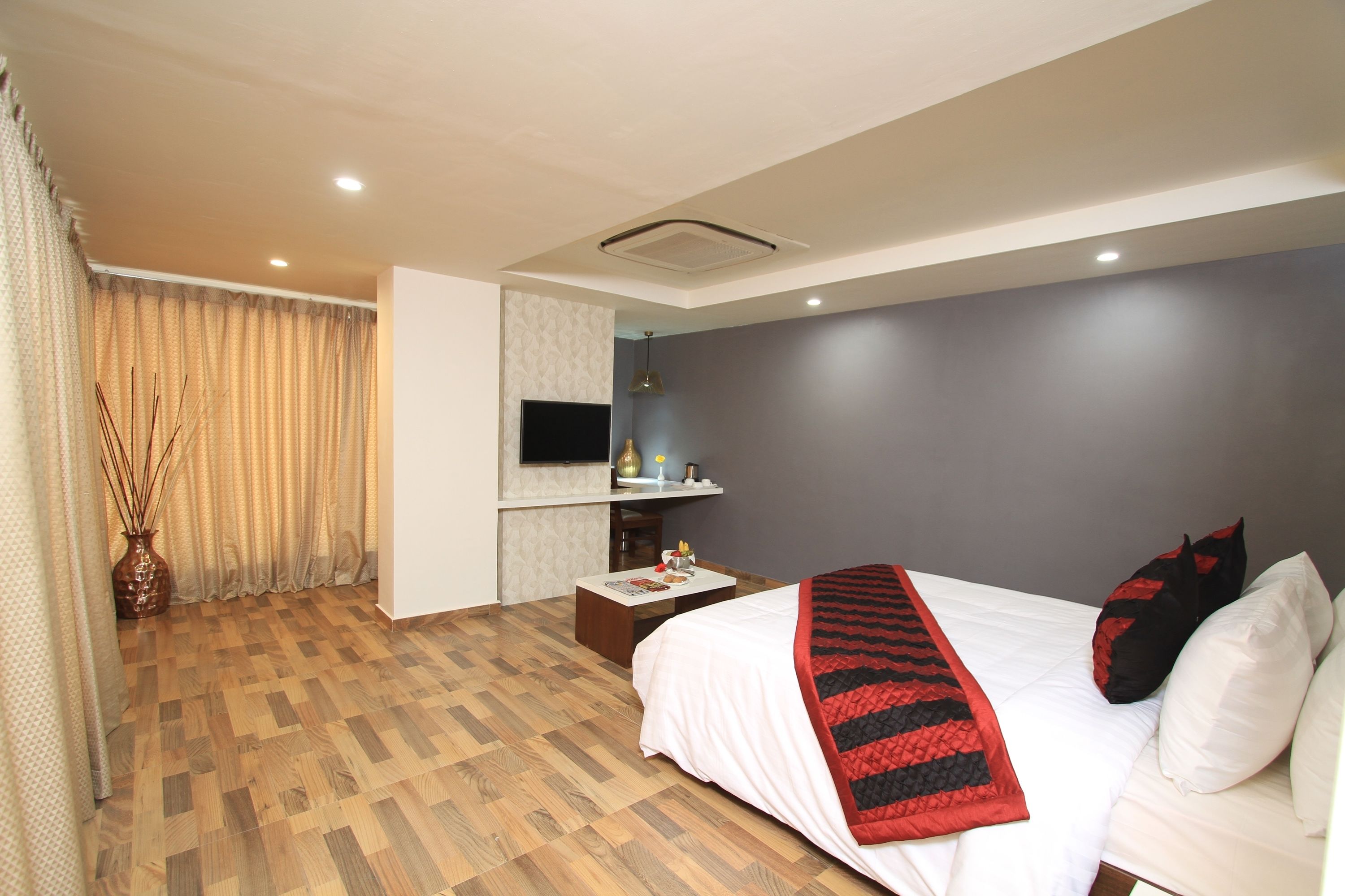 Una habitación de hotel moderna con una cama grande, un televisor de pantalla plana, un escritorio pequeño y un ventanal con cortinas.