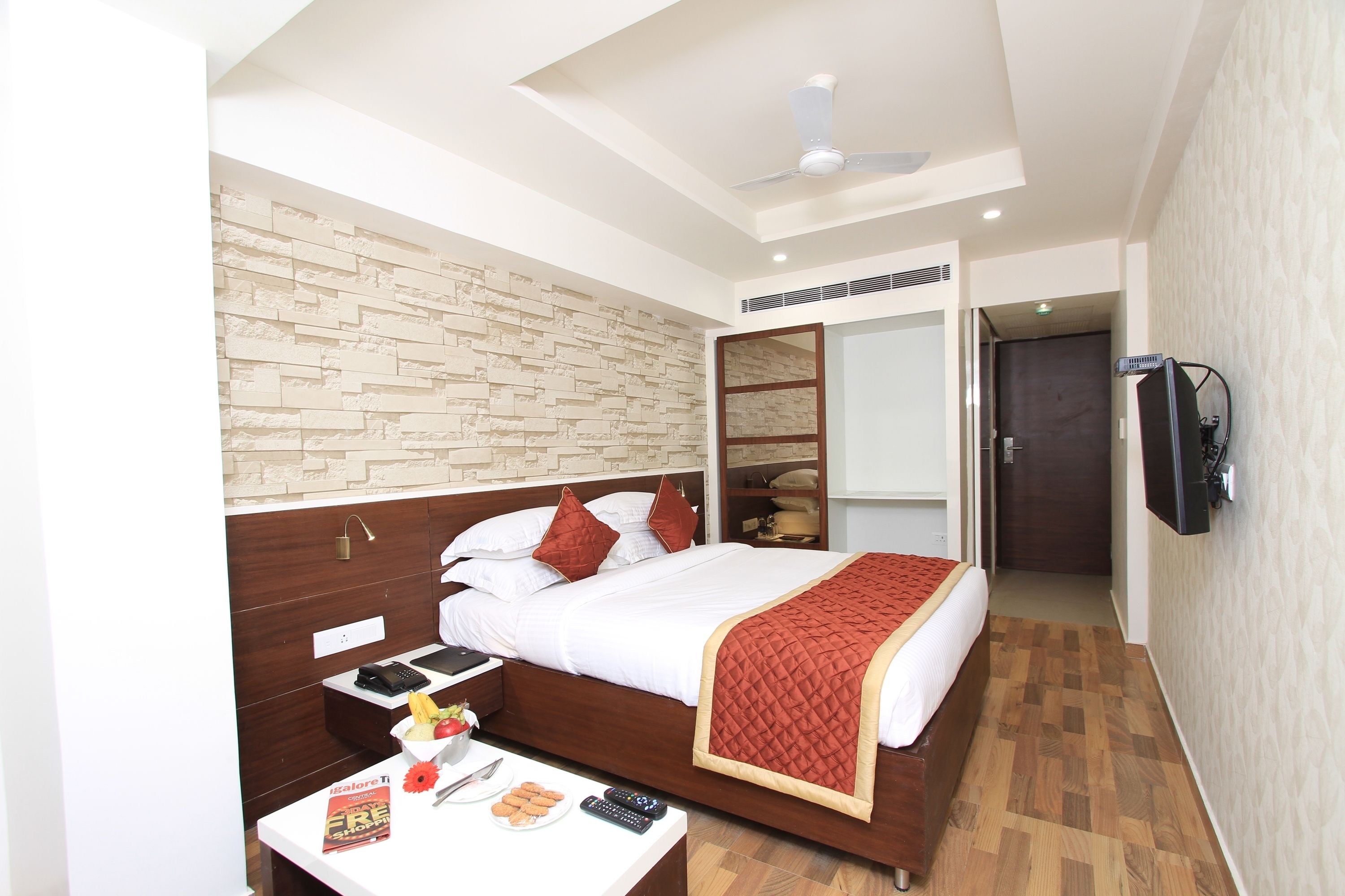 A hotel room with a bed, bedside table, and a television mounted on the wall.