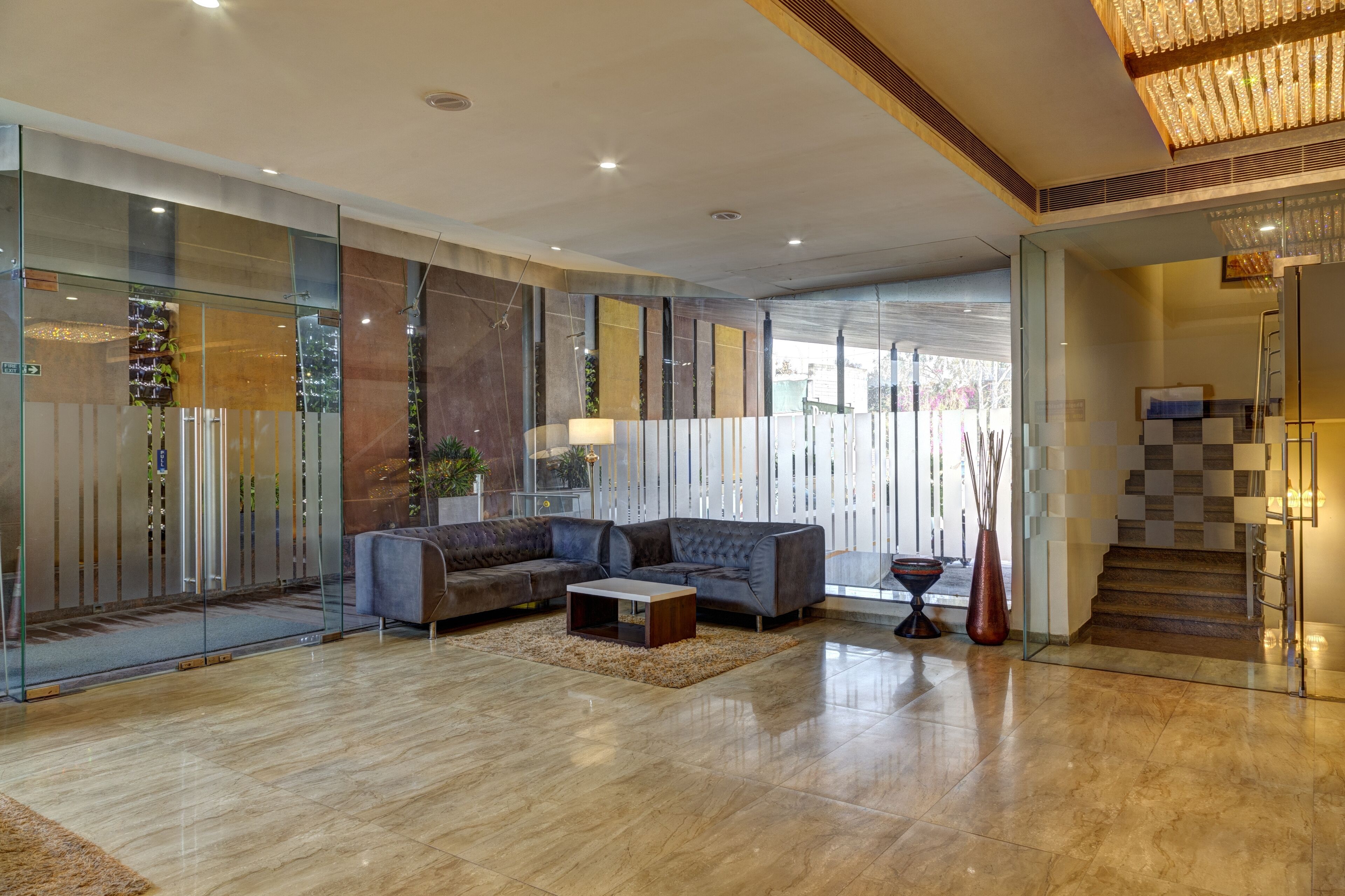 A modern hotel lobby with a sectional sofa, a coffee table, and a glass partition with vertical blinds.