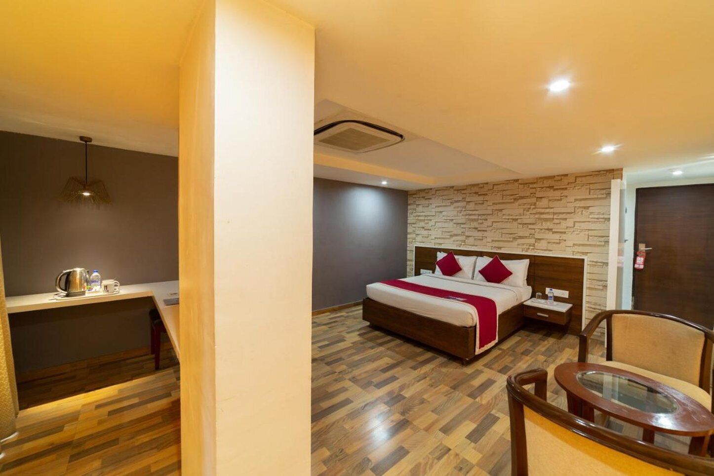 A hotel room with a wooden floor, a bed with a red bedspread, a nightstand, a chair, and a small table.
