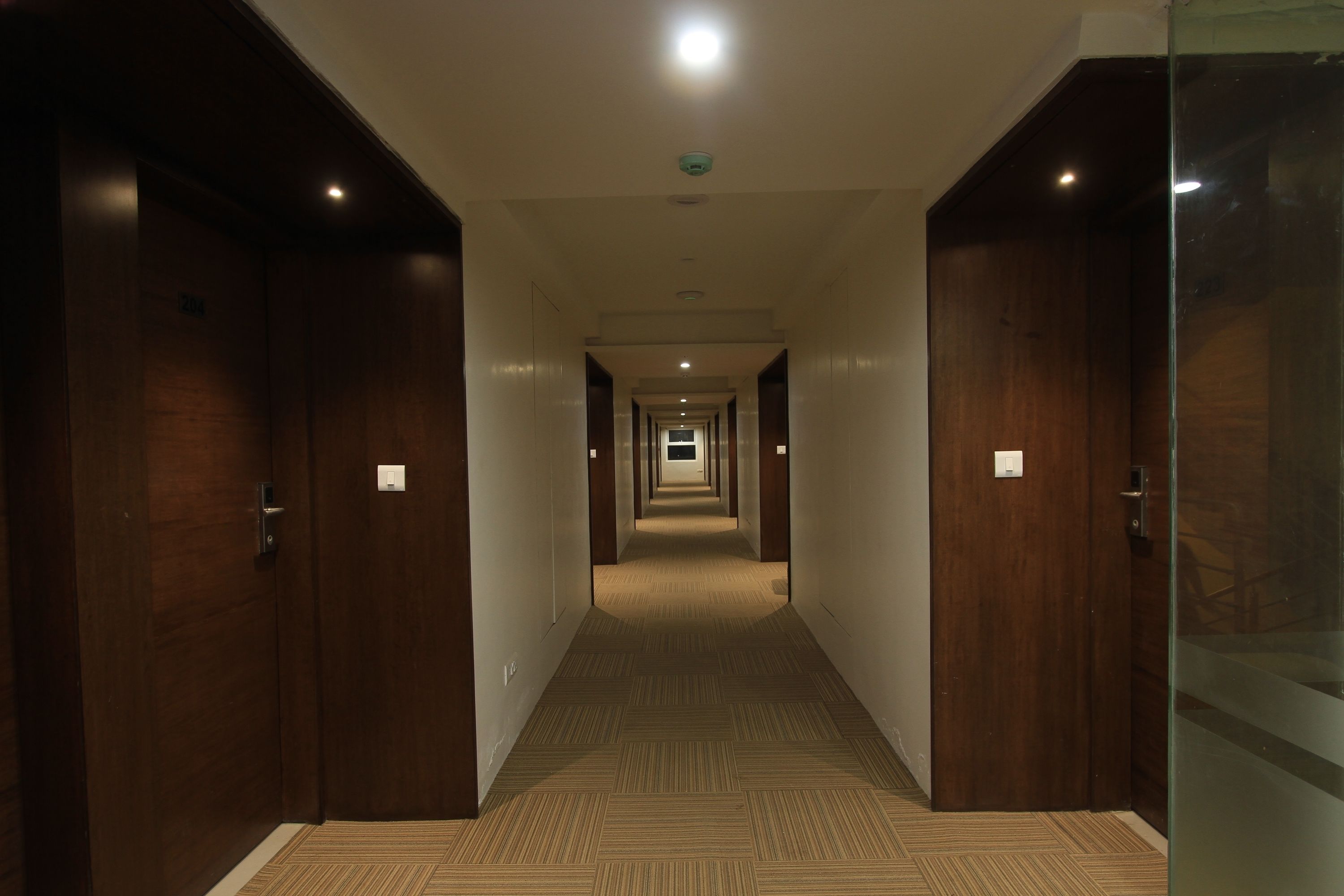 A long, narrow hallway with wooden doors on both sides, leading to a bright end.