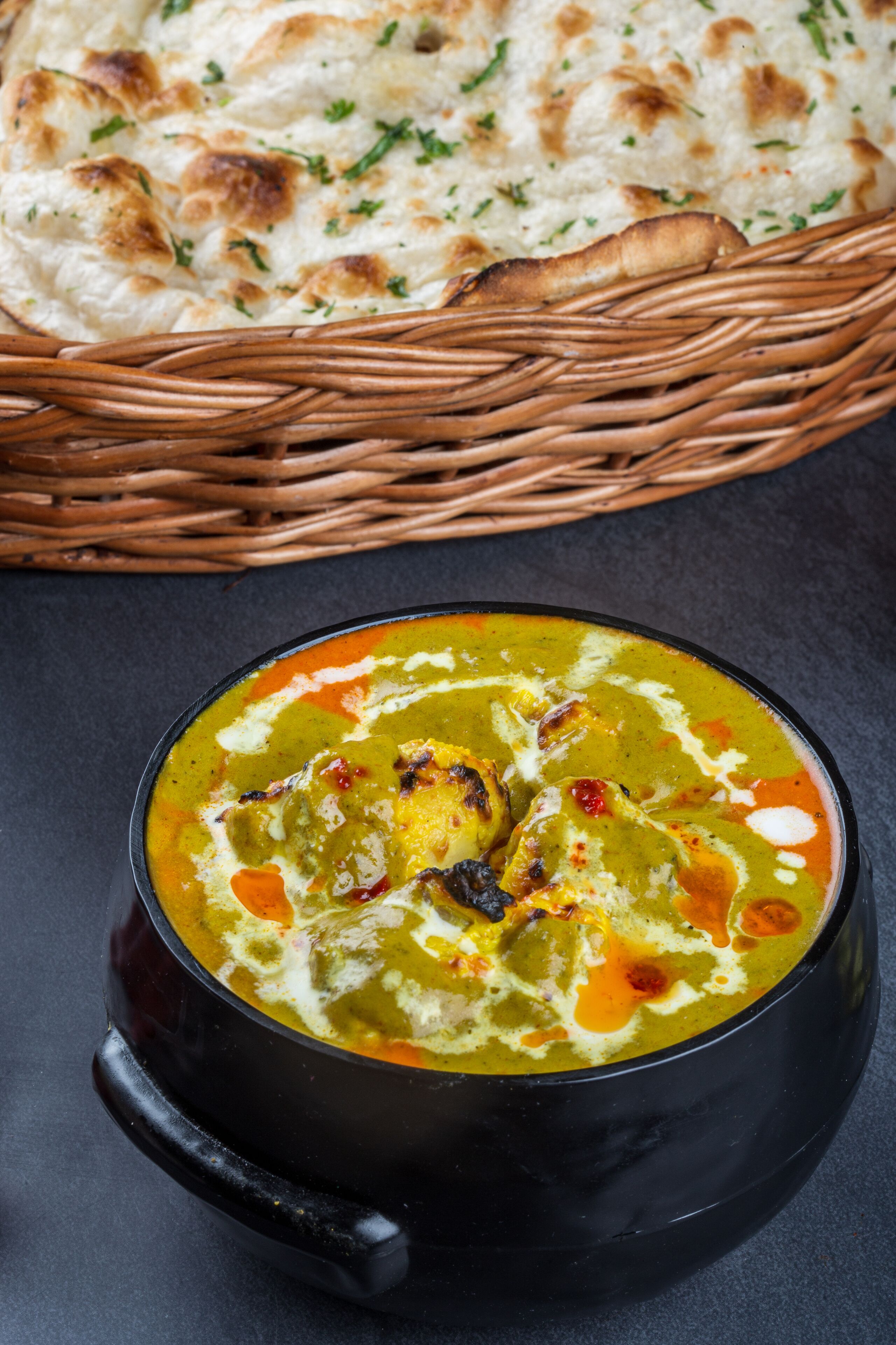 A bowl of curry with naan bread in the background.