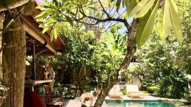 A poolside area with a wooden deck, a red chair, and white orchids. - D'uma Residence (Denpasar)