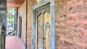 A corridor with a wooden door and a stone statue. - D'uma Residence (Denpasar)
