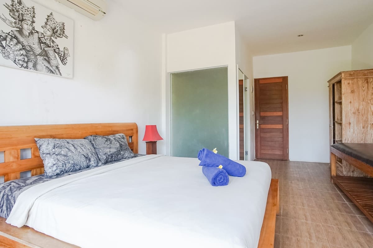 A hotel room with a wooden bed, a red lamp, a door, and a wooden cabinet.