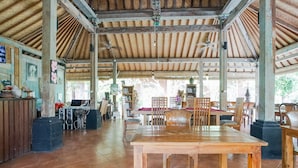 A spacious indoor area with a high wooden ceiling, tiled floor, and several wooden tables and chairs. - D'uma Residence (Denpasar)