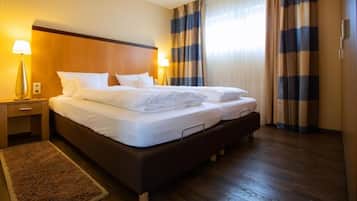 Quarto de hotel com uma cama grande, duas mesas de cabeceira, uma luminária e vista para o exterior através das cortinas.