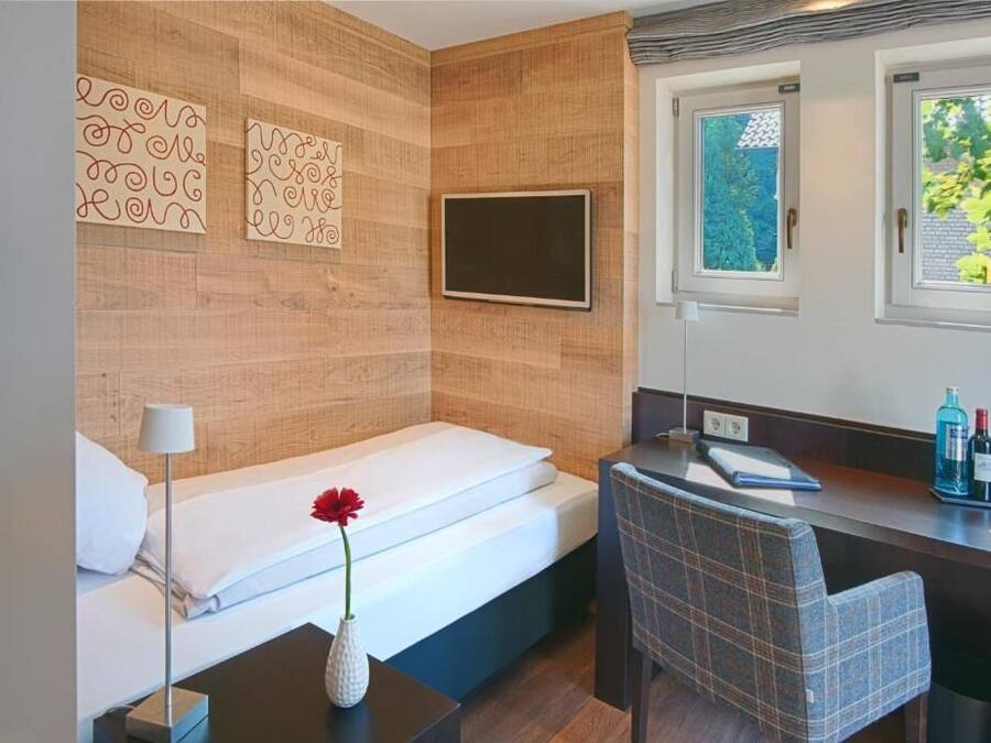 A modern hotel room with a bed, a desk, a chair, a TV, and a window with a view of trees.