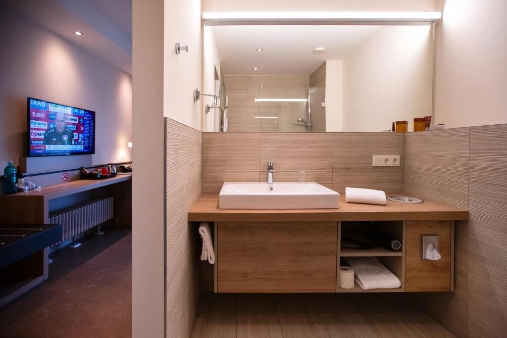 A modern bathroom with a wooden vanity, a large mirror, and a television mounted on the wall.