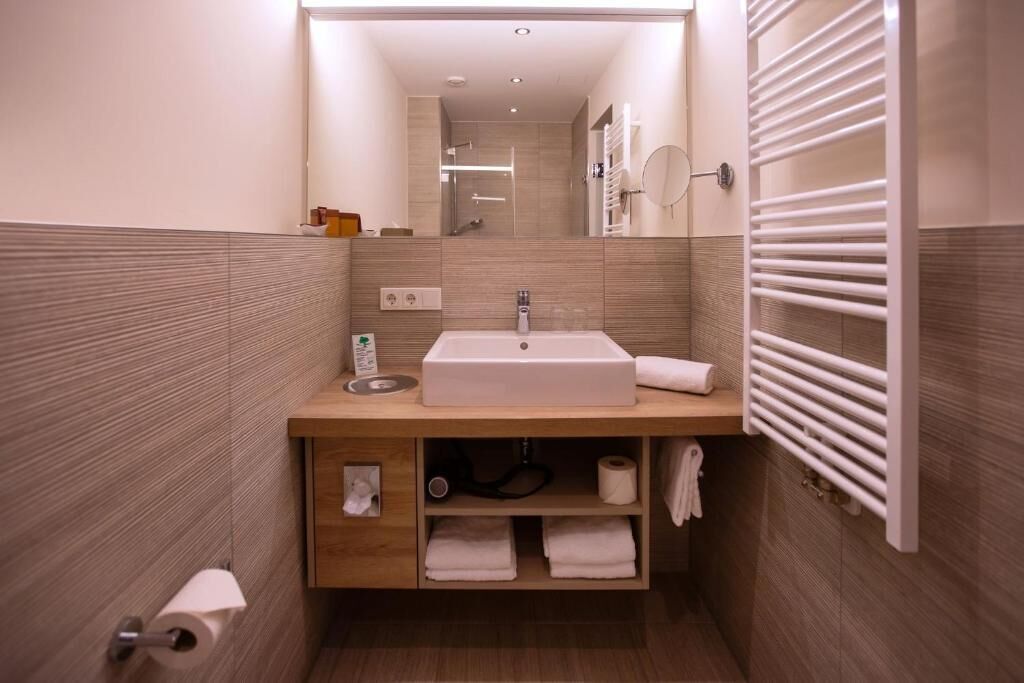 A compact bathroom with a sink, mirror, towel rack, and a toilet.