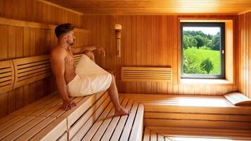 A sauna room with wooden benches and a window offering a view of greenery.