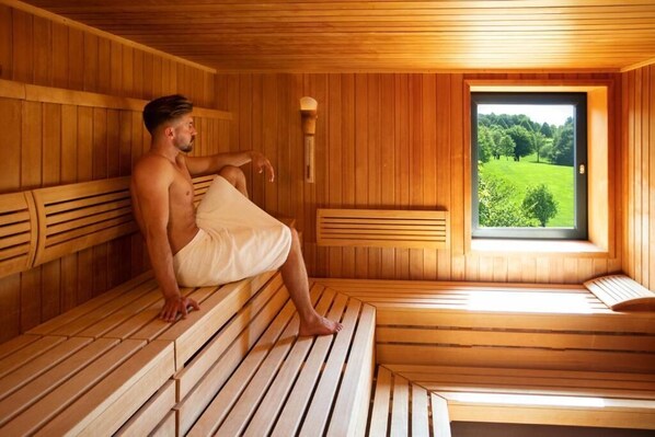 Una sala de sauna con bancos de madera y un ventanal con vistas al follaje.