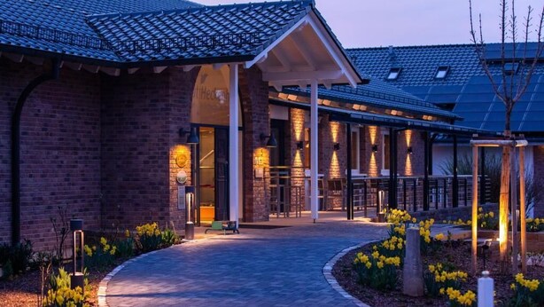 A brick building with a covered entrance and a pathway leading to it. - Gut Heckenhof Hotel & Golfresort (Eitorf)