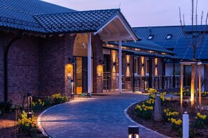 A brick building with a covered entrance and a pathway leading to it. - Gut Heckenhof Hotel & Golfresort (Eitorf)