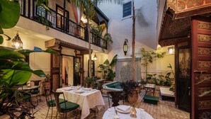 A courtyard with tables and chairs set up for dining, surrounded by potted plants and a decorative fountain. - Riad Dar El Souk (Marrakech)