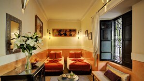A hotel room with two beds, a sofa, a small table, and a vase of flowers. - Riad Dar El Souk (Marrakech)