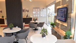 A modern hotel lobby with round tables, grey chairs, and potted plants. - Al Mawasim Al Arbaeah Serviced Apartments (Tabuk)
