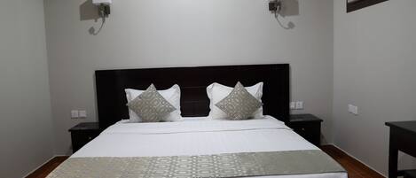 A neatly made bed with a patterned bedspread, two bedside tables with lamps, and a wall-mounted air conditioning unit.