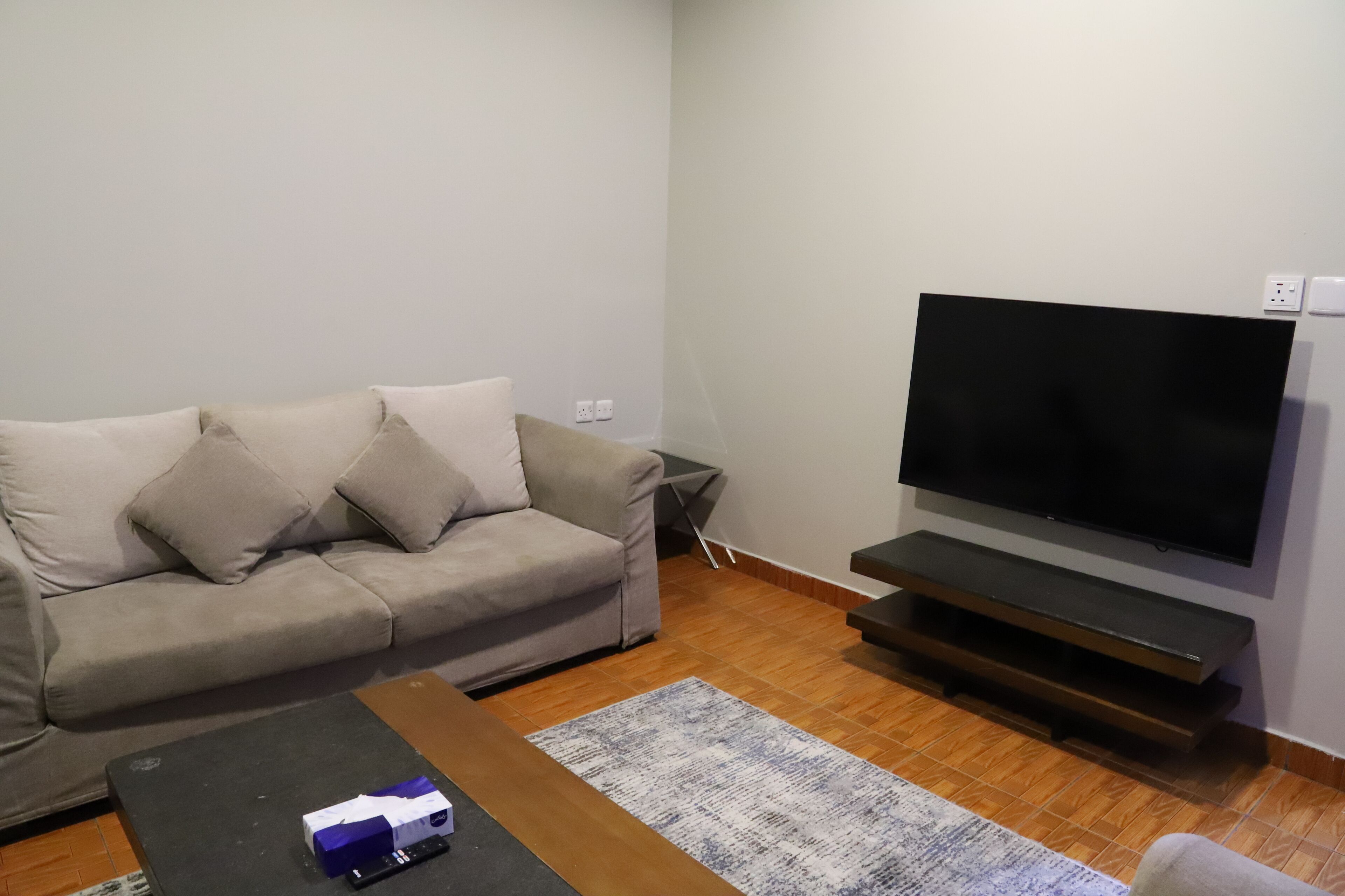 A living room with a sofa, a coffee table, a flat-screen TV, and a wooden floor.