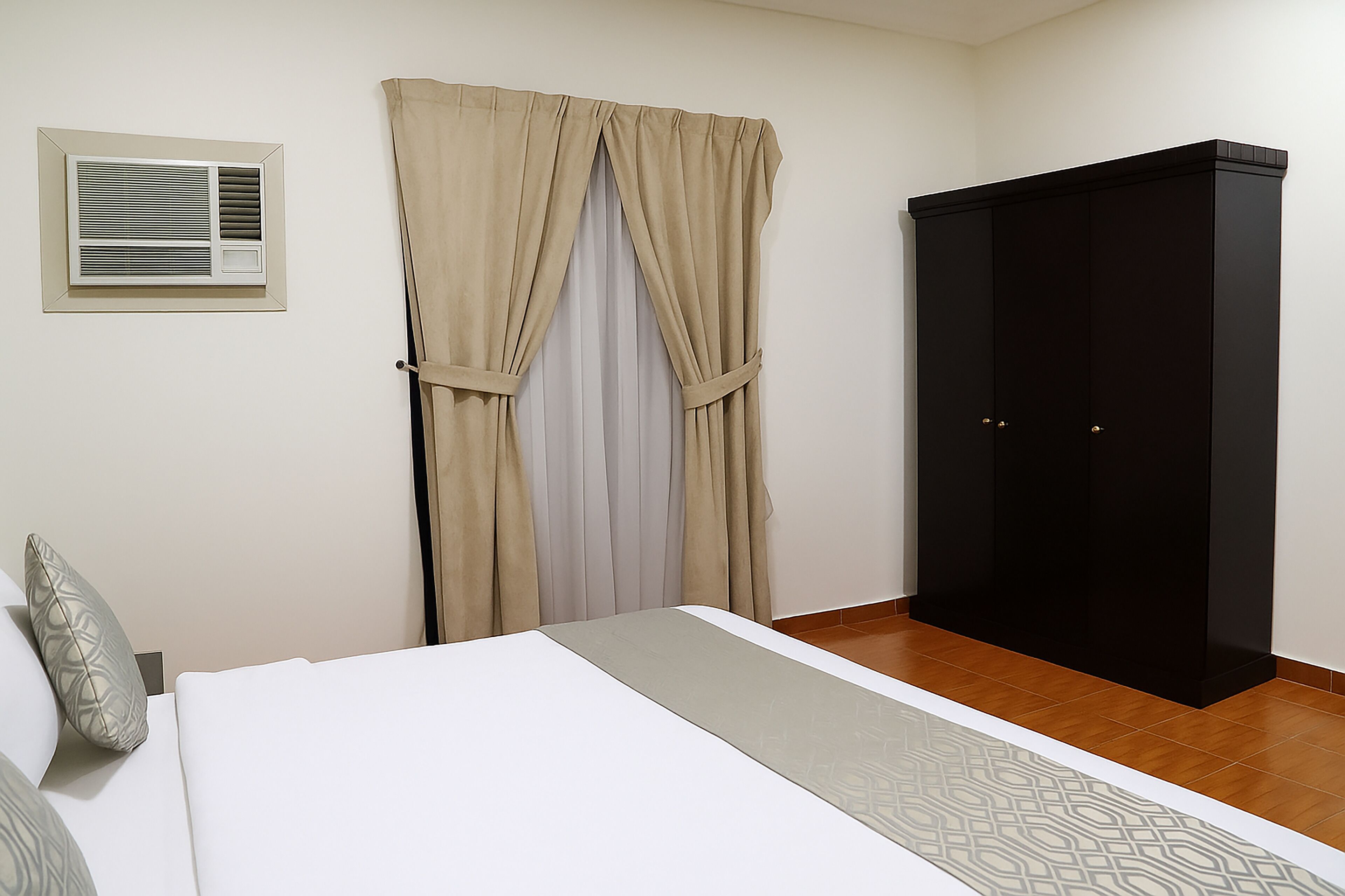A bedroom with a bed, a wardrobe, a window with curtains, and an air conditioning unit.