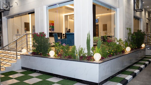 A reception area with a glass partition, a staircase with metal railings, and a planter with various plants and decorative lights. - Al Mawasim Al Arbaeah Serviced Apartments (Tabuk)