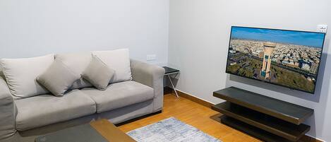 A living room with a grey sofa, a coffee table with a tissue box, a flat-screen TV on a stand, and a wooden floor.