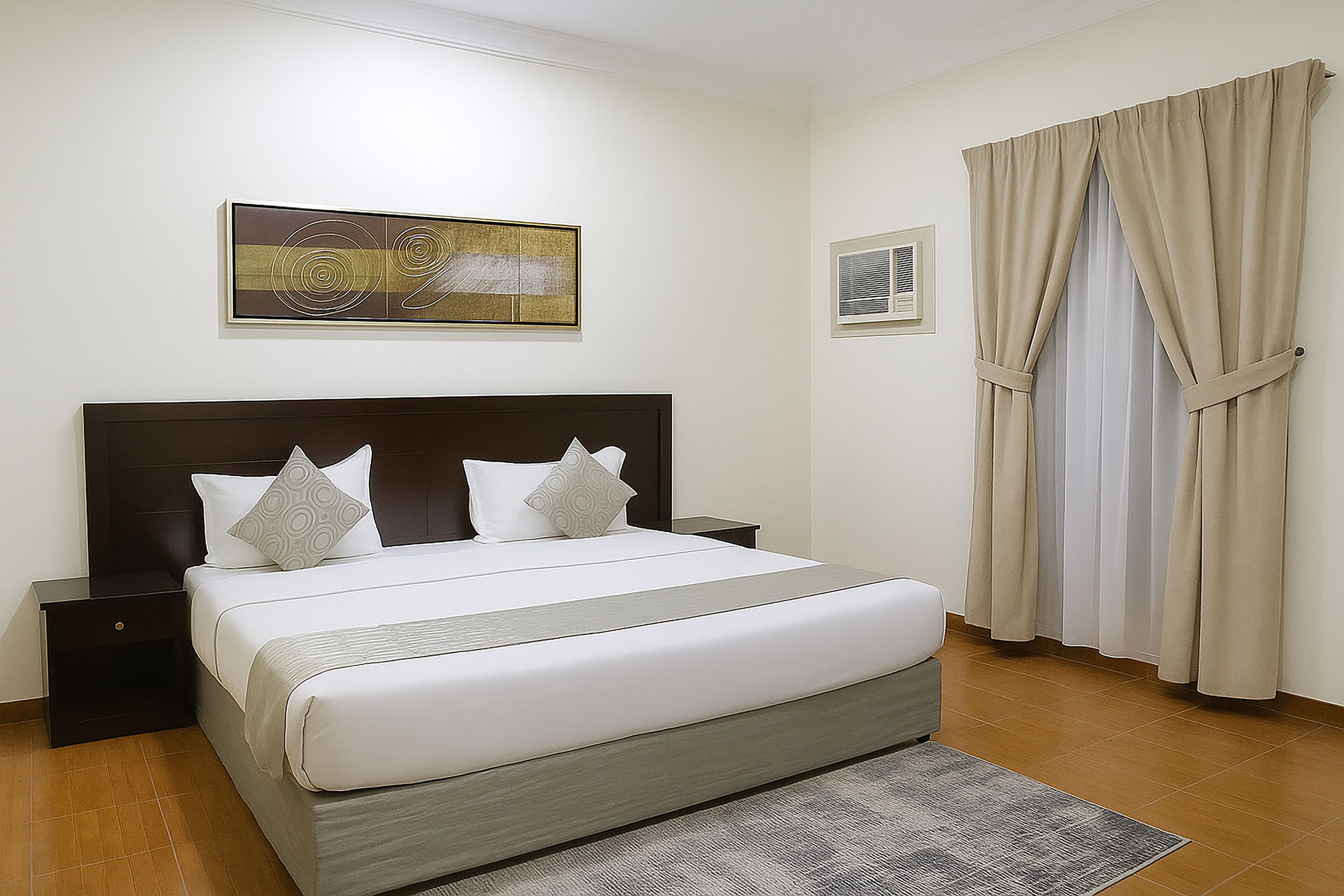 A neatly arranged bedroom with a large bed, a headboard, a nightstand, a framed picture on the wall, and a window with curtains.
