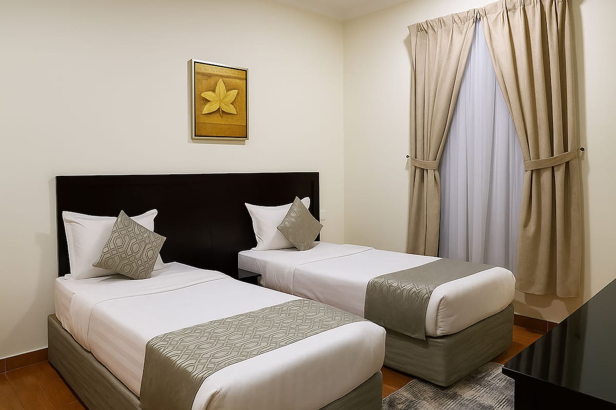 A hotel room with two beds, a black headboard, a framed artwork on the wall, and beige curtains.