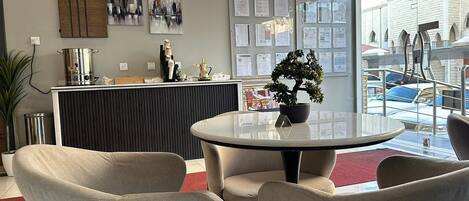 A reception area with a round table, chairs, a potted plant, a reception desk, and a view of the outside.