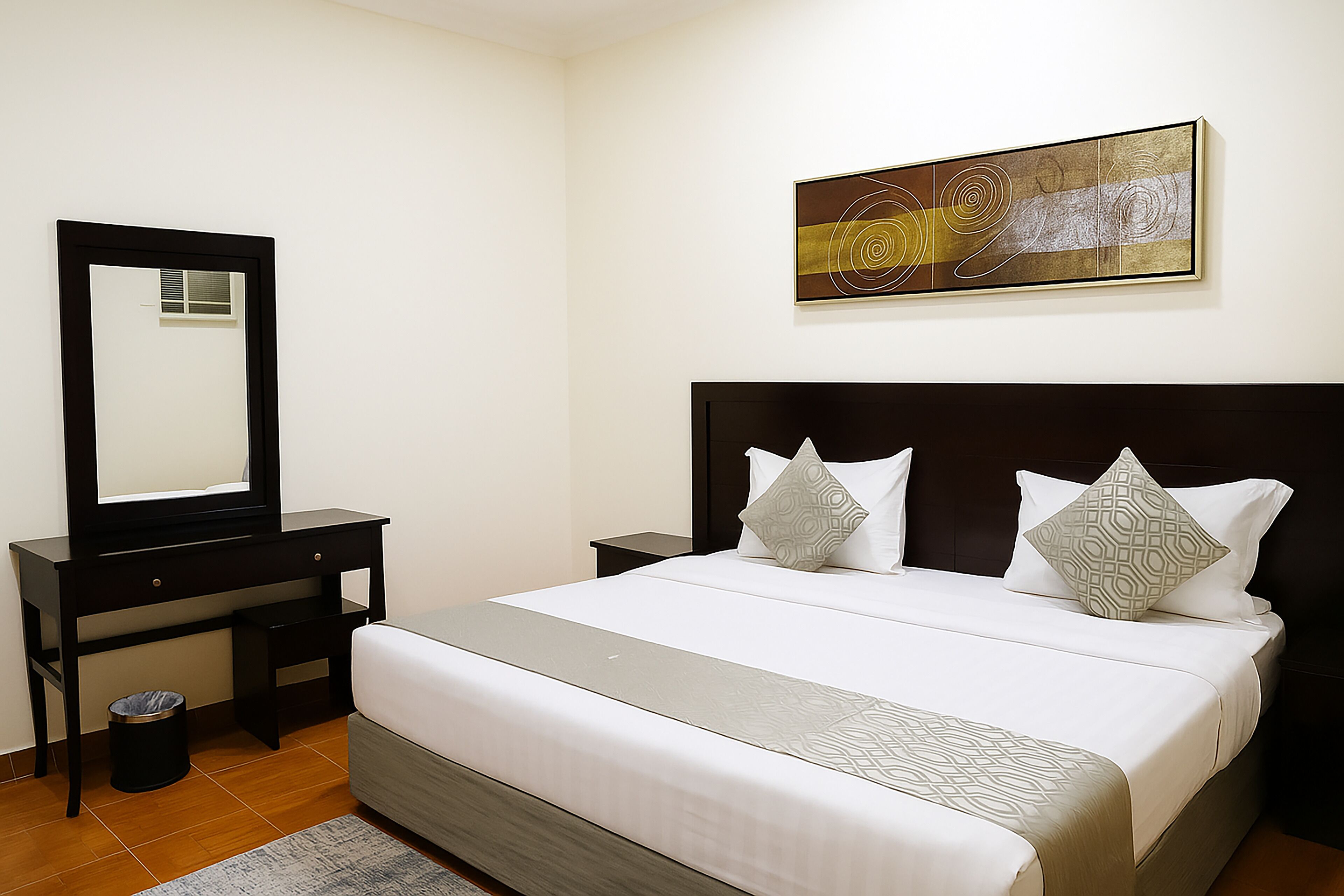 Ein Hotelzimmer mit einem Bett, einem Schreibtisch, einem Stuhl, einem Mülleimer und einem Wandbild.