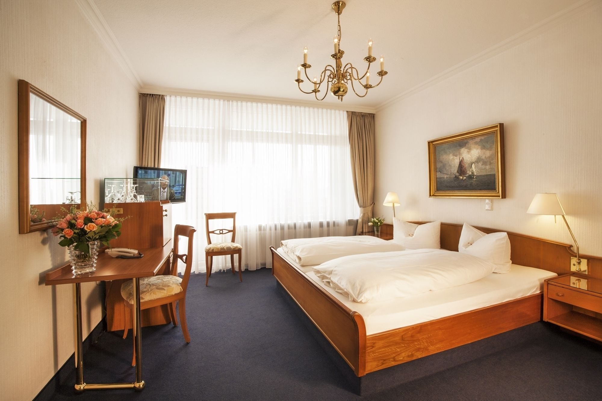 Une chambre d’hôtel avec un grand lit, un bureau avec une télévision, une chaise, une lampe de bureau et un tableau au mur.