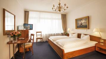 Une chambre d’hôtel avec un grand lit, un bureau avec une télévision, une chaise, une lampe de bureau et un tableau au mur.