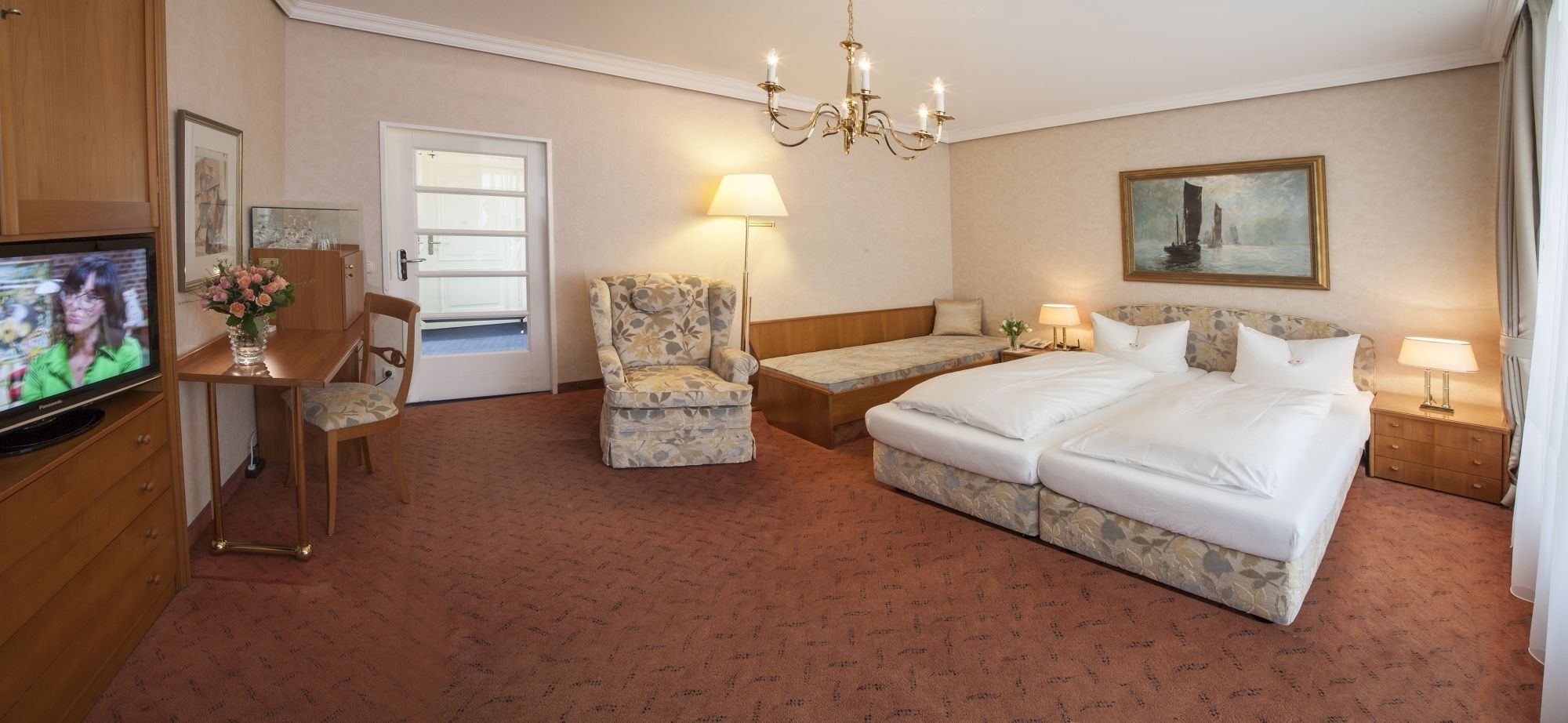 A hotel room with a bed, a chair, a desk, a television, and a painting on the wall.
