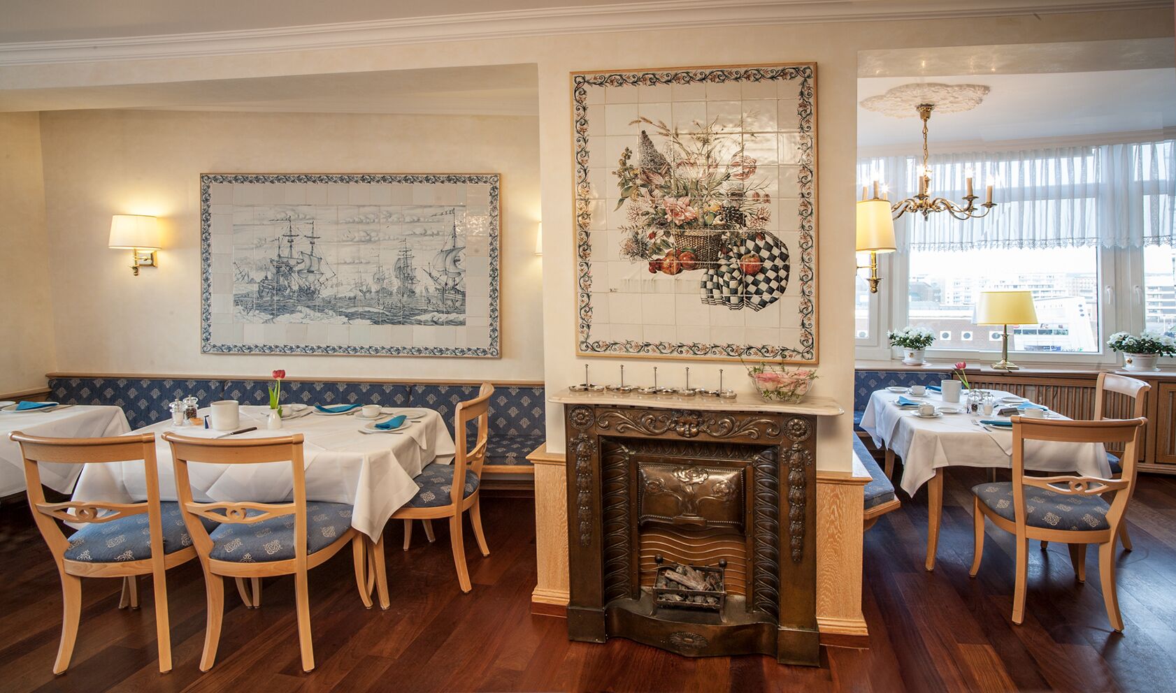 Comedor con sillas y mesas de madera, chimenea y obras de arte en las paredes.
