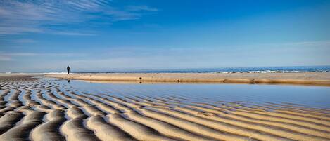 A beach with rippled sand patterns and a person walking.