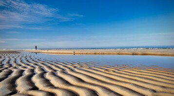 Ein Strand mit wellenartigen Sandmustern und einer Person, die spazieren geht.