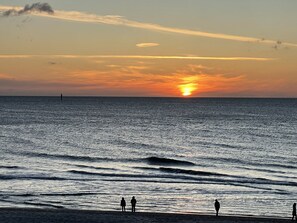 Ein Sonnenuntergang über dem Meer mit einigen Personen am Strand.