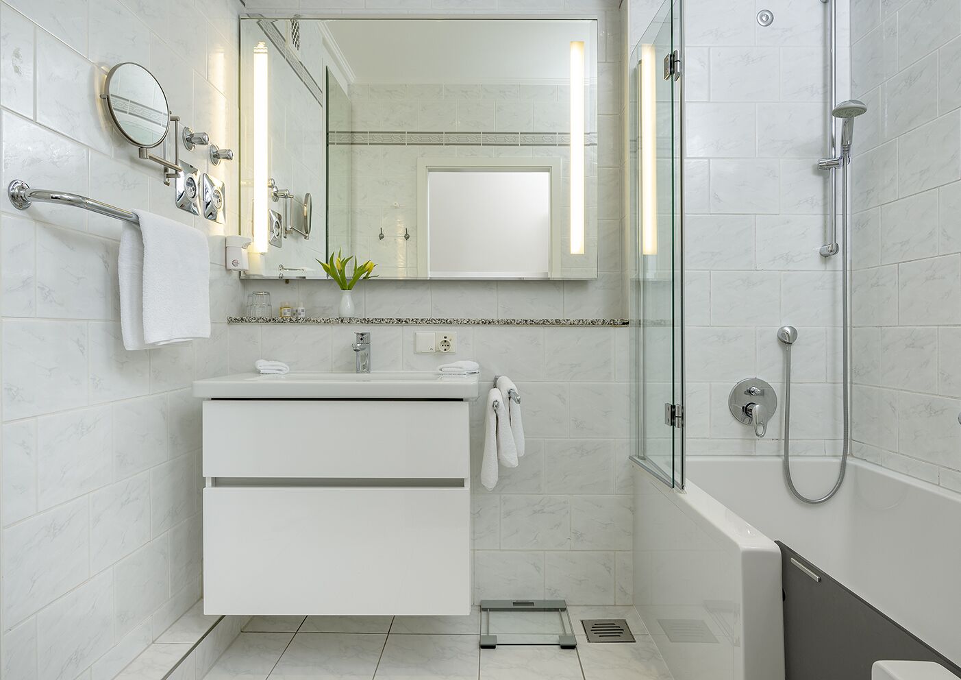 A modern bathroom with a glass shower enclosure, a white vanity with a mirror, and a small plant on the countertop.