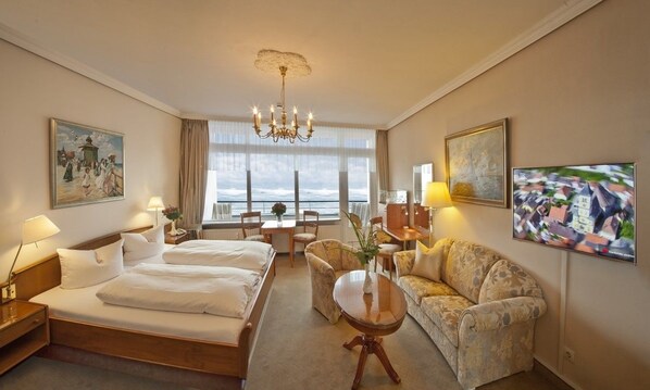 Ein Hotelzimmer mit einem großen Bett, einer Couch, einem Schreibtisch und Meerblick.