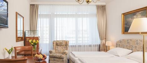 Habitació d'hotel amb llit, escriptori i cadira, una petita butaca, un penjallum i un quadre a la paret.