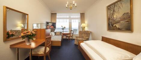 A hotel room with a bed, a desk with a chair, a sofa, a TV, and a painting on the wall.