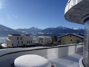 En snötäckt balkong med utsikt över snöklädda berg och byggnader i bakgrunden.