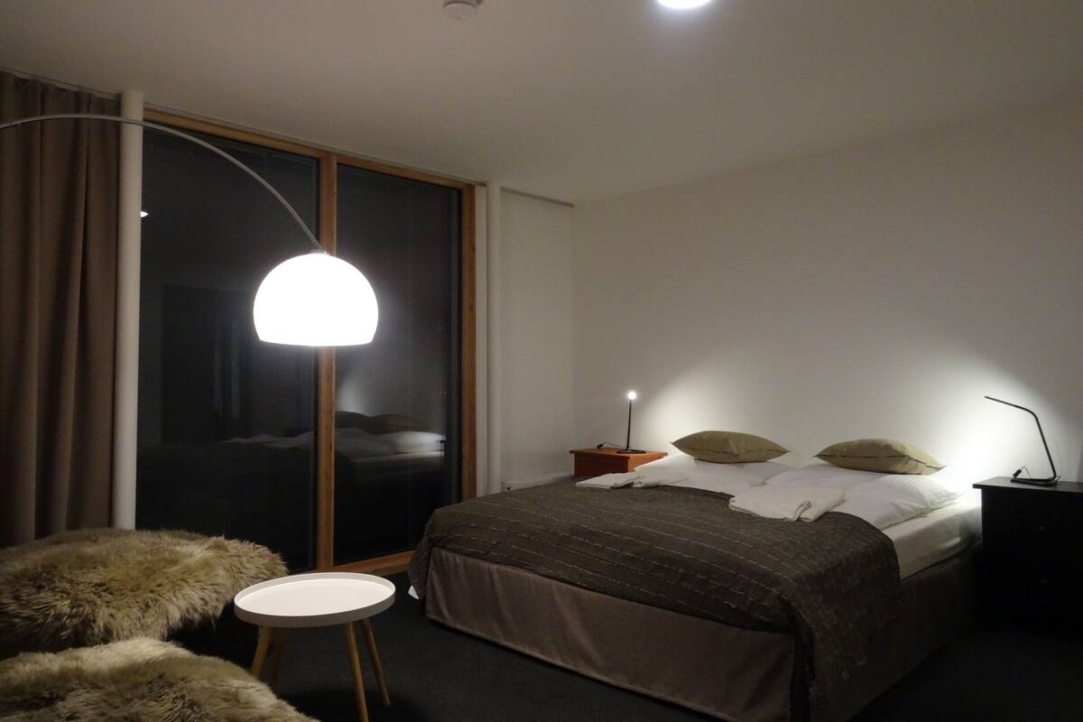 A modern bedroom with a large bed, a round table, and a floor lamp.