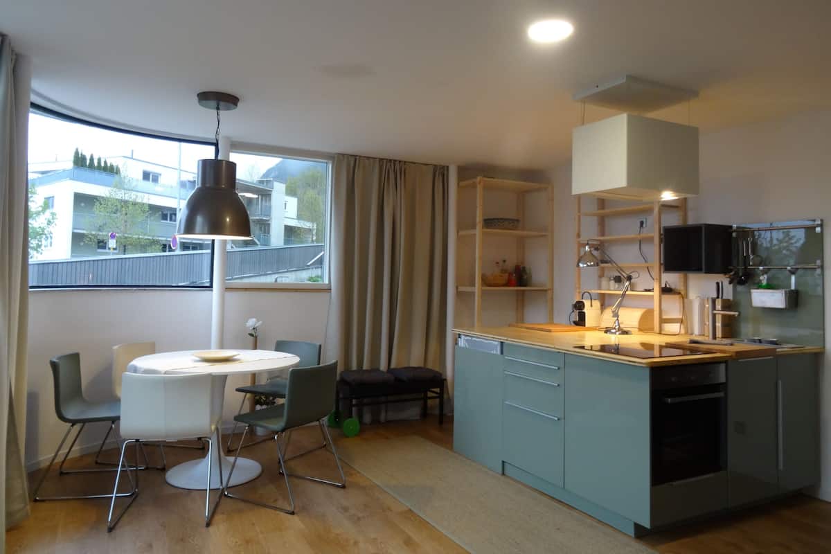 A modern kitchen with a dining area, wooden cabinets, and a large window with curtains.