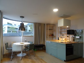 Una cocina moderna con comedor, armarios de madera y un amplio ventanal con cortinas.