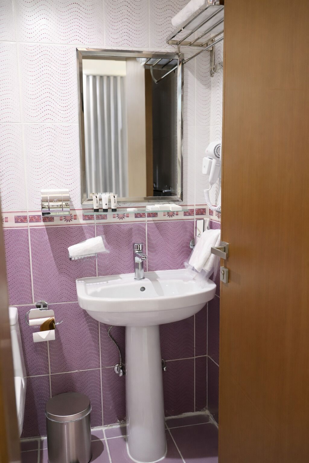 Een badkamer met een wit wastafelmeubel, een spiegel, een handdoekhouder en een prullenbak.