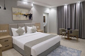 A modern hotel room with a large bed, bedside tables, a desk with chairs, a bathroom, and a large window with curtains. - Ajnihat alshamal for Serviced Apartments Serviced  (Tabuk)