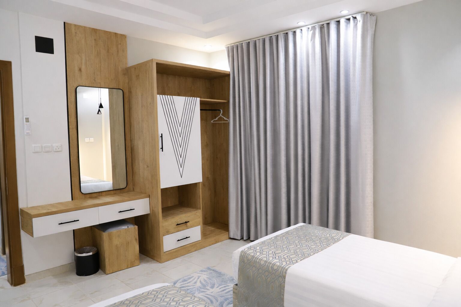 A modern bedroom with a bed, a wardrobe with a mirror, a hanging closet, and a window with curtains.