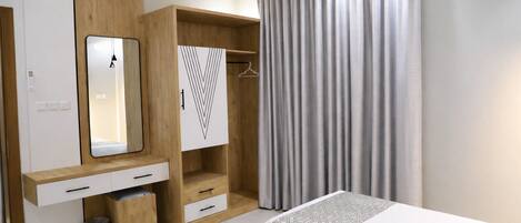 A modern bedroom with a bed, a wardrobe with a mirror, a hanging closet, and a window with curtains.