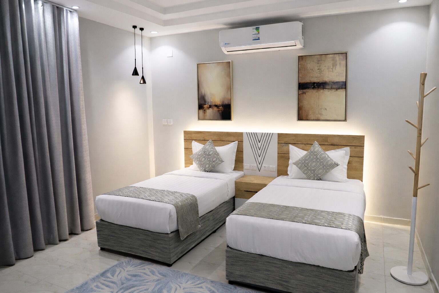 A modern hotel room with two beds, grey curtains, a wooden headboard, and a large abstract painting on the wall.